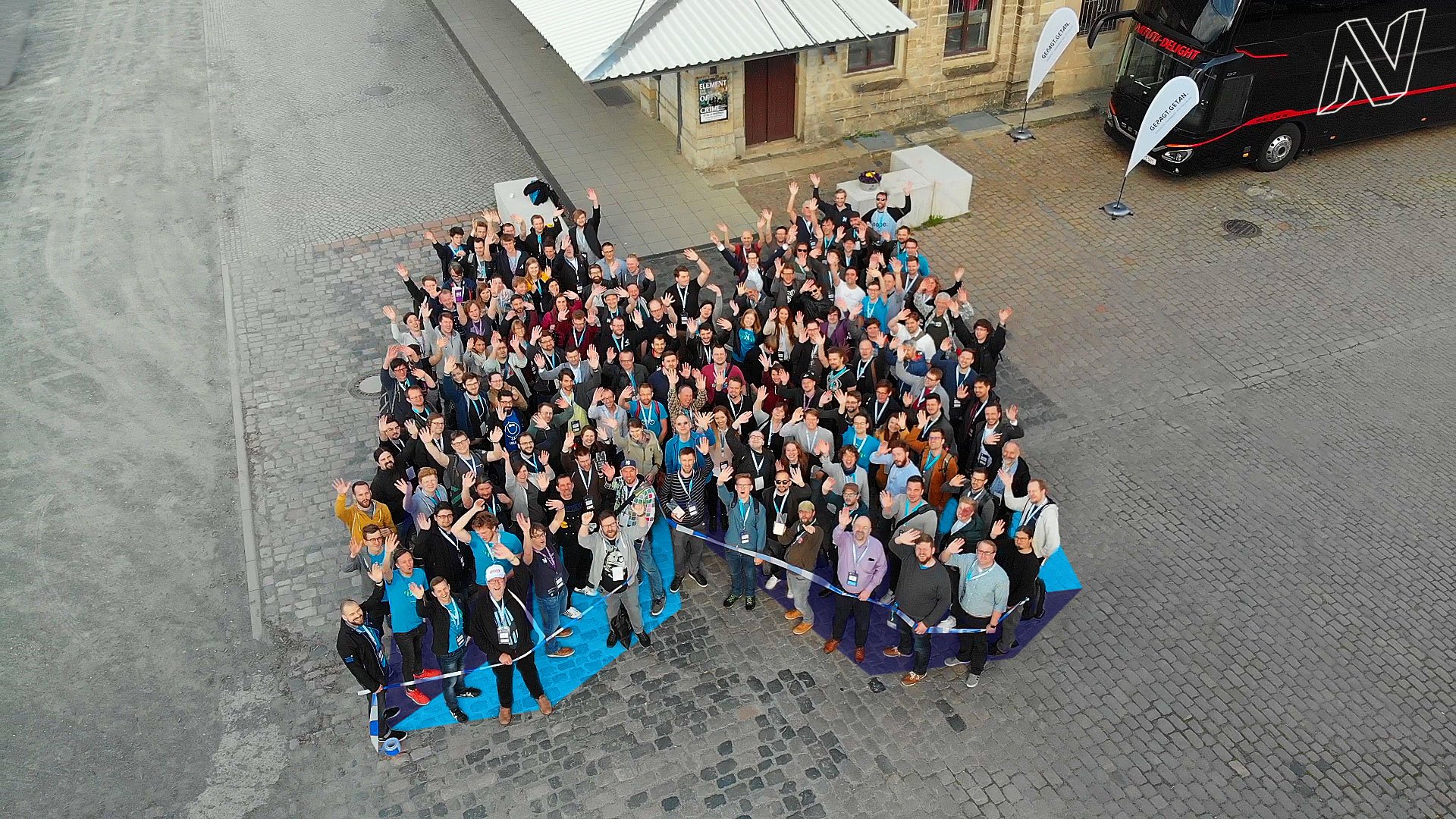 Neos conference attendees form the project logo outside the conference location